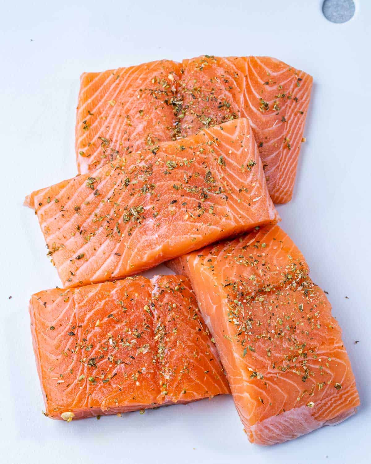 Four salmon filets seasoned on cutting board.