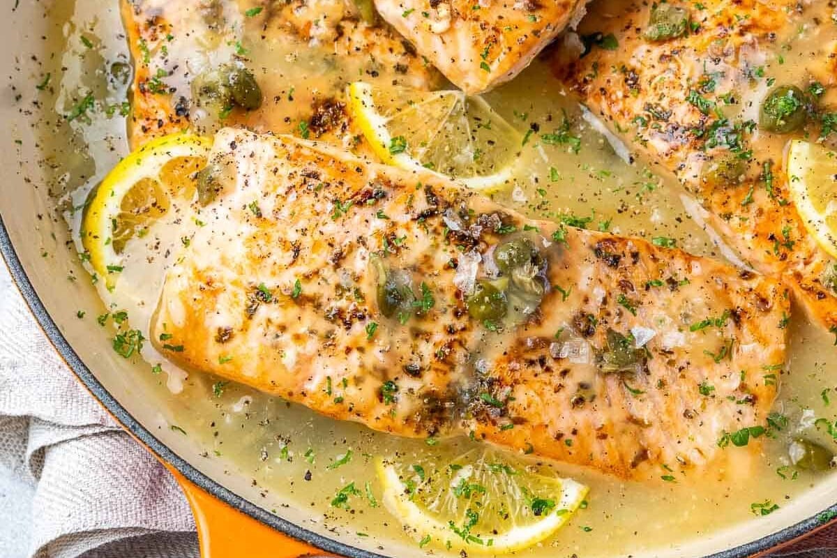 Skillet of salmon piccata garnished with parsley.