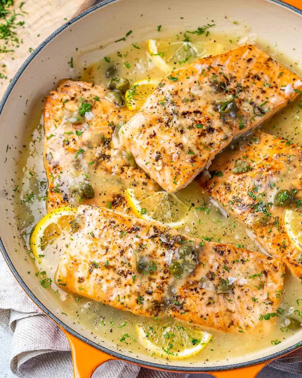 Skillet of salmon piccata garnished with parsley.