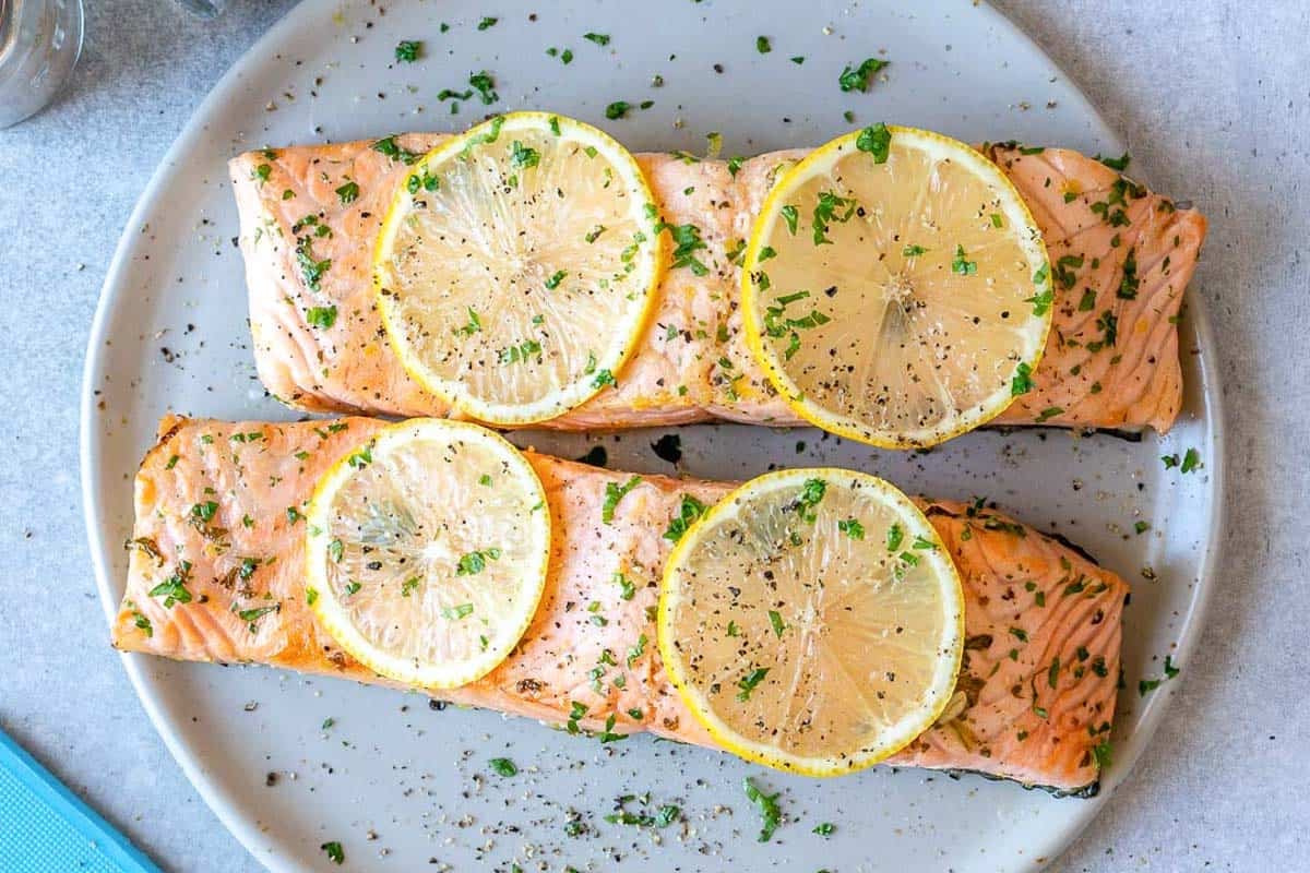 two baked salmon topped with lemon slices on a plate.
