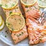 flaked lemon garlic salmon on a plate with sliced lemon rounds over it.