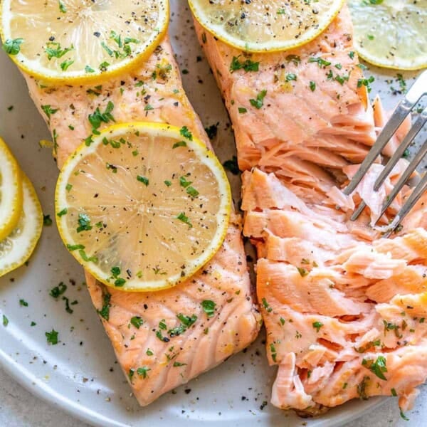 flaked lemon garlic salmon on a plate with sliced lemon rounds over it.