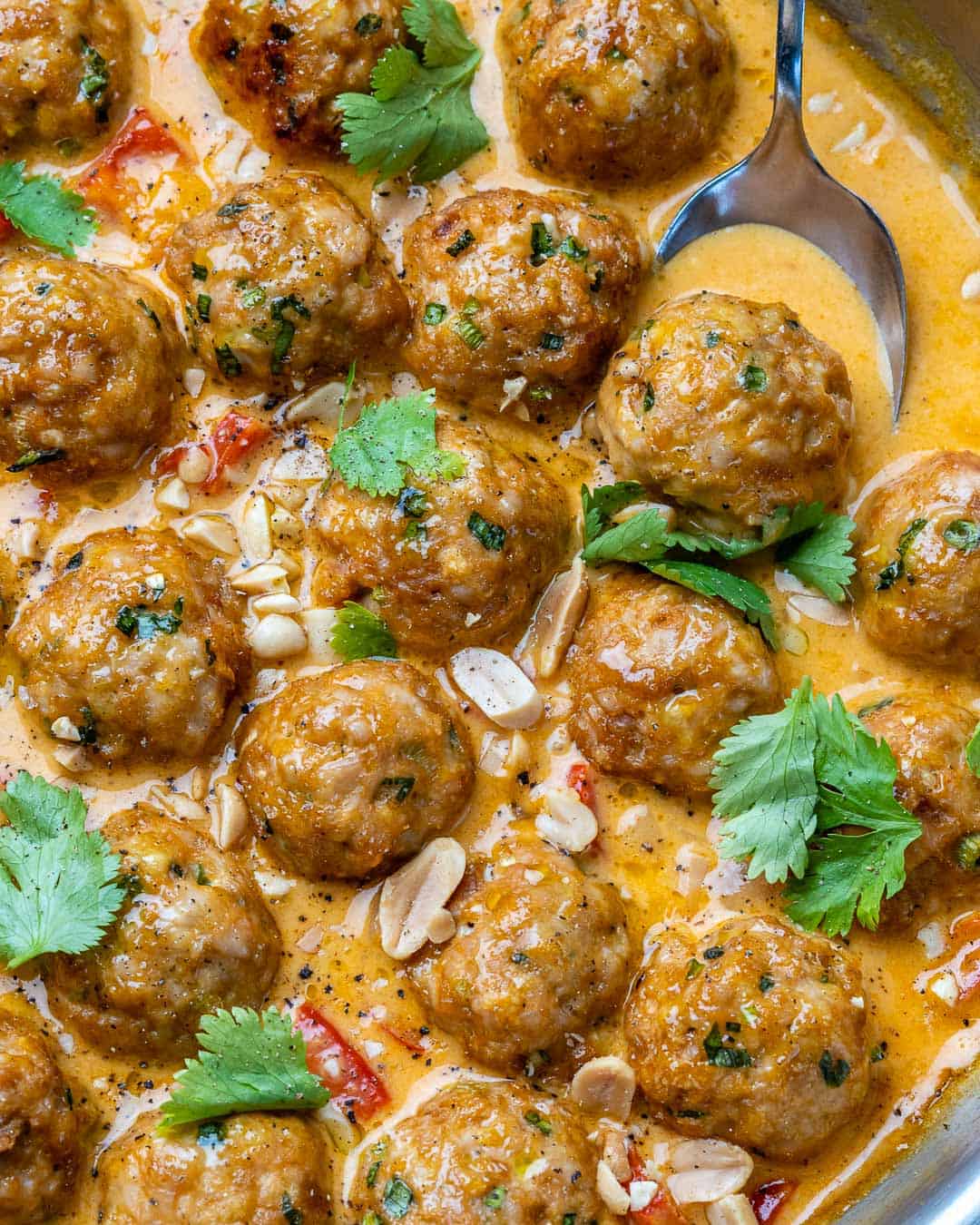 spoon in a pan getting a serving of turkey meatballs in curry sauce.