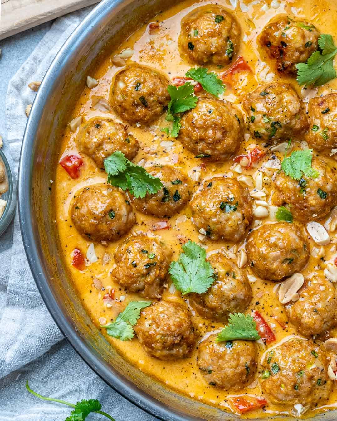 Turkey meatballs in a curry sauce in a stainless steel round pan with cilantro and chopped peanuts garnish.