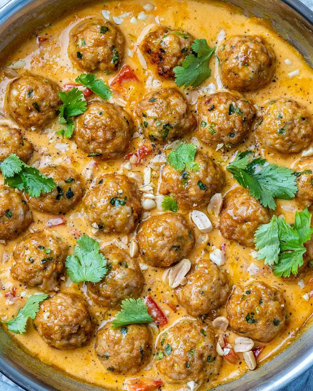 Turkey meatballs in a curry sauce in a stainless steel round pan with cilantro and chopped peanuts garnish.