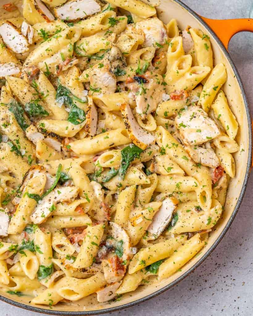 Orange skillet filled with chicken and pasta with spinach