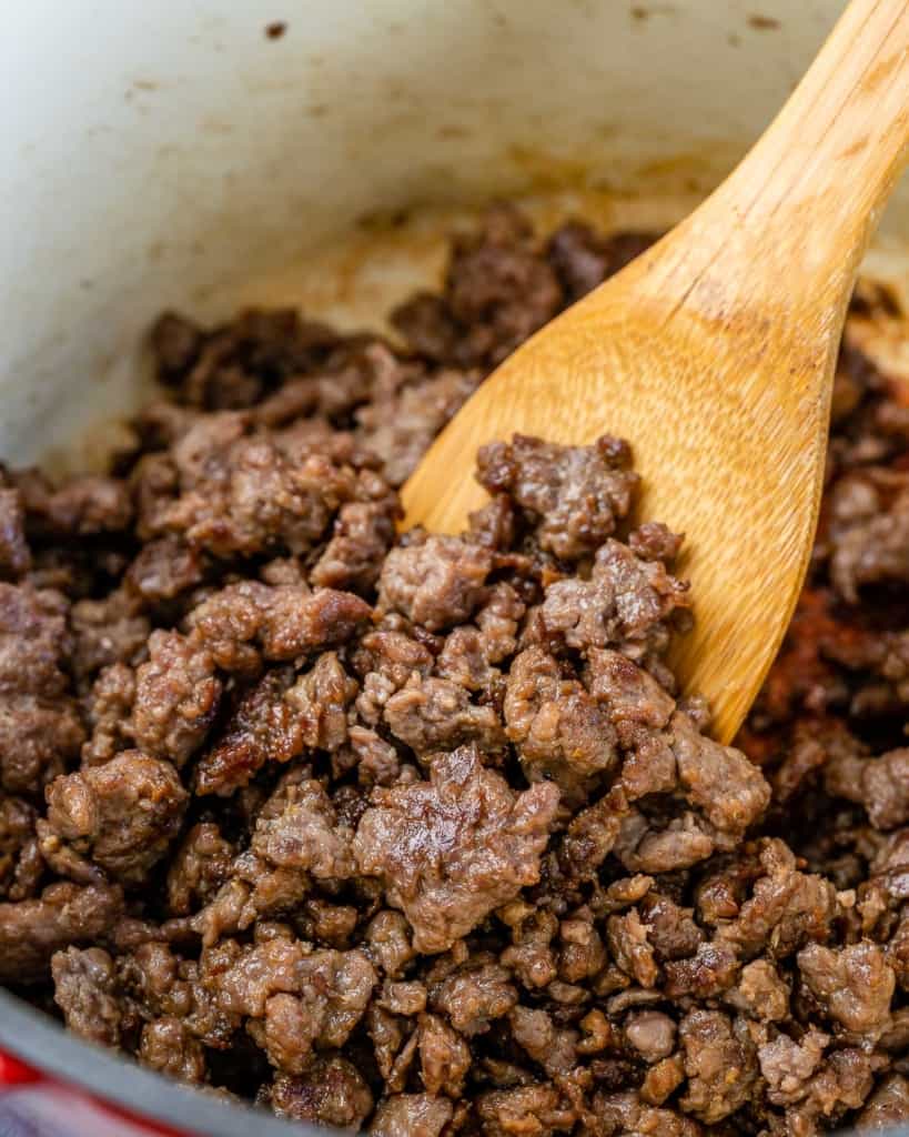 Ground beef browned in pot with wooden spoon.