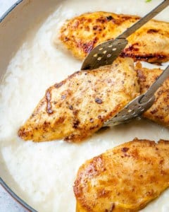 chicken breast being placed over creamy sauce