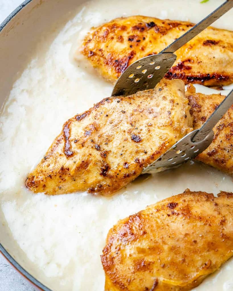 chicken breast being placed over creamy sauce 
