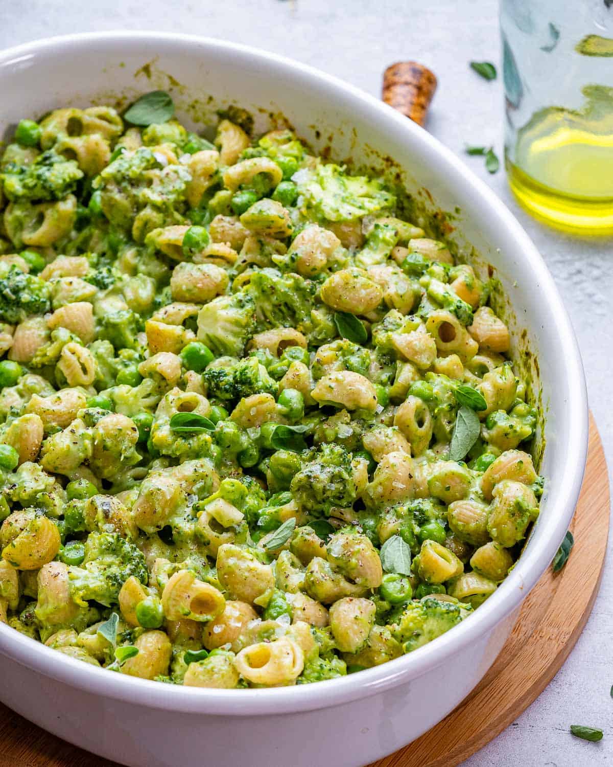 Oval baking dish of green mac and cheese with ingredients on the side.