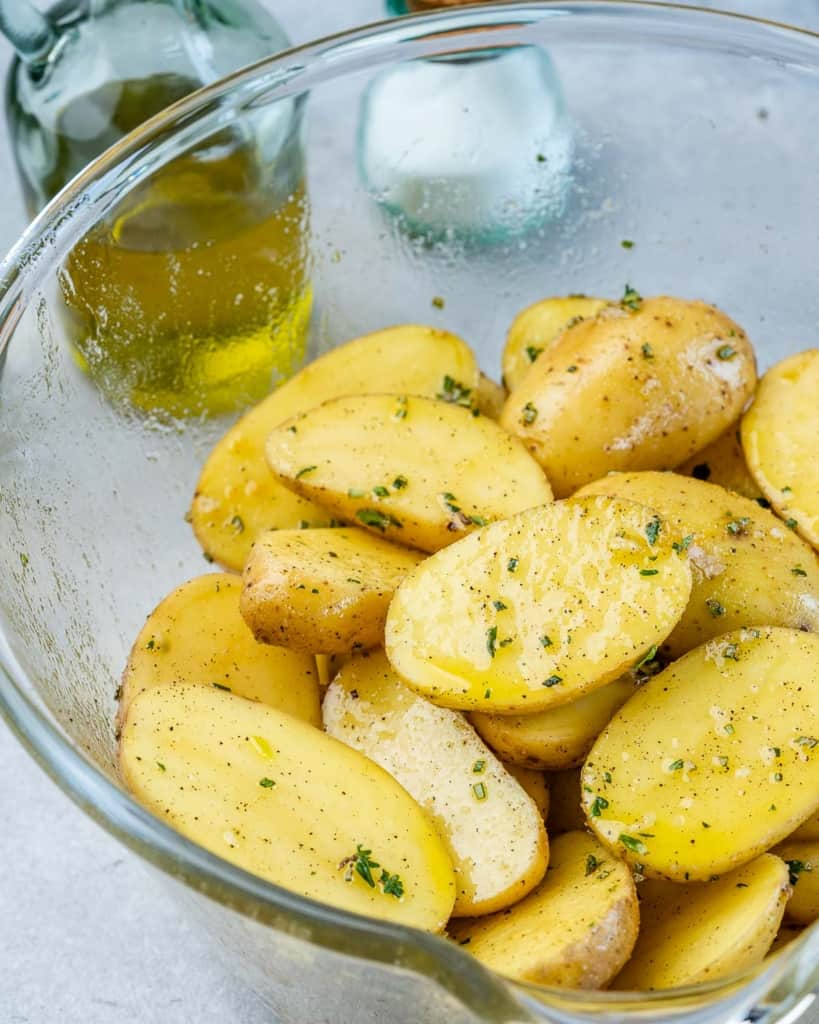 raw potatoes coated with herbs and oil in a bowl