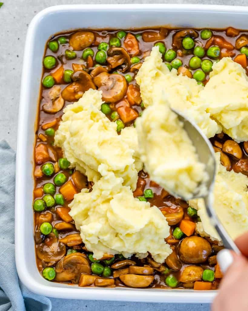 Spoon piling mashed potatoes on top of vegetable filling.