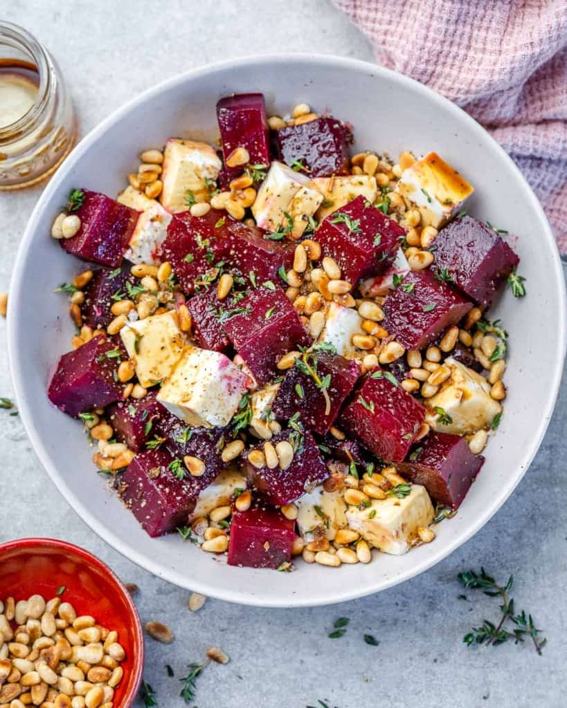 Roasted beet salad in white bowl with pine nuts and pink linen