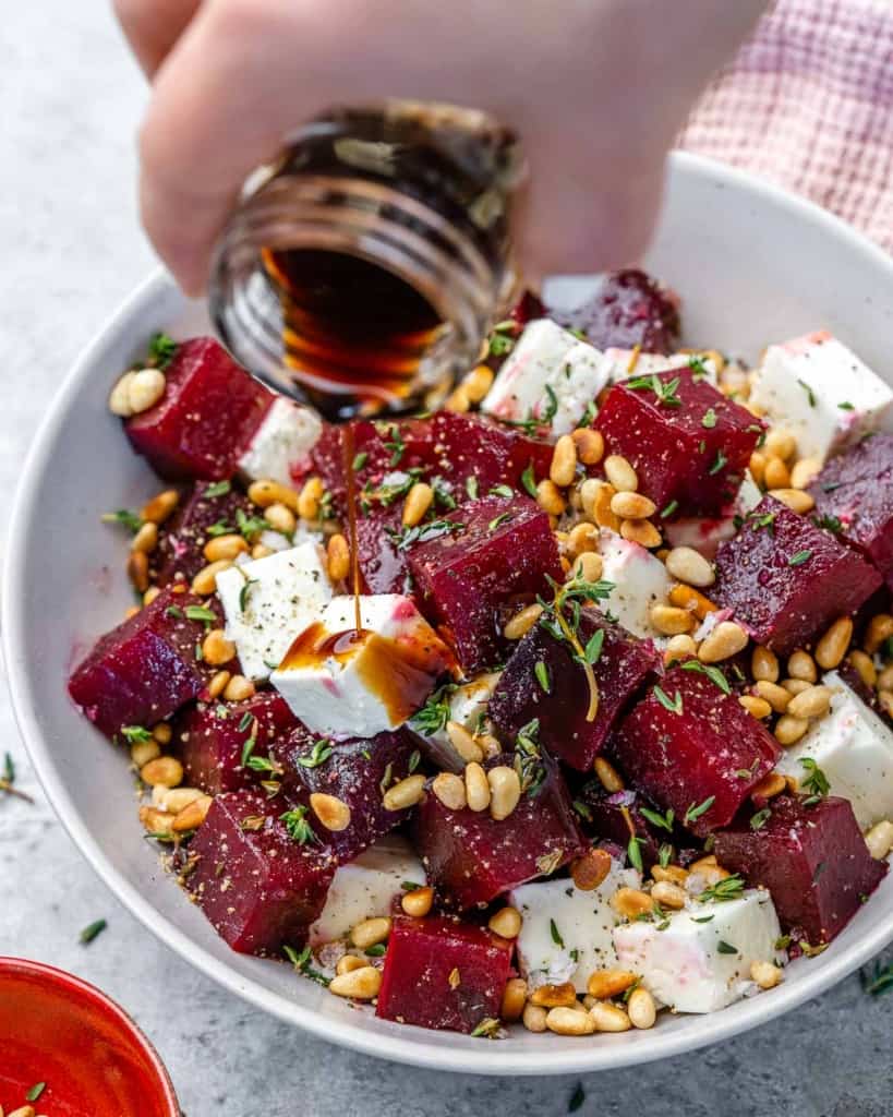 Balsamic vinegar being poured over roasted beet salad in white bowl