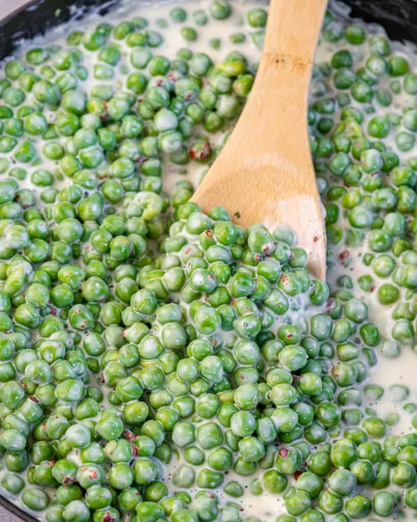 creamy peas in a skillet with wooden spoon in it