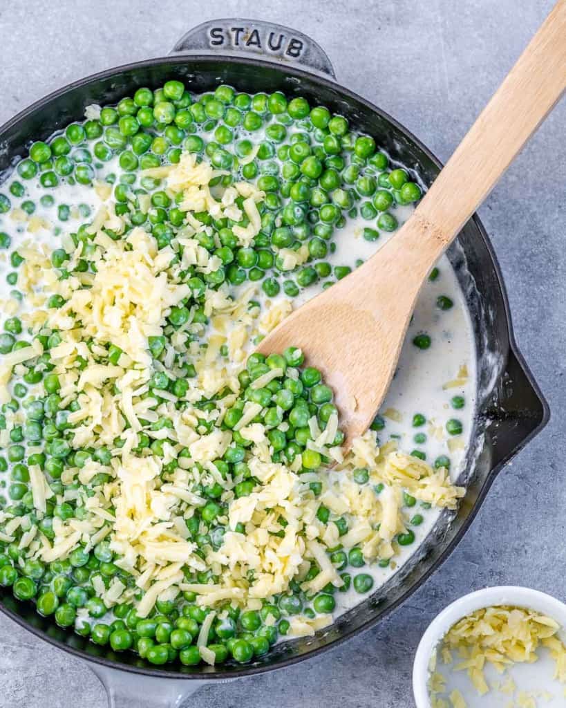 skillet with peas, milk, cheese being stirred with a wooden spoon