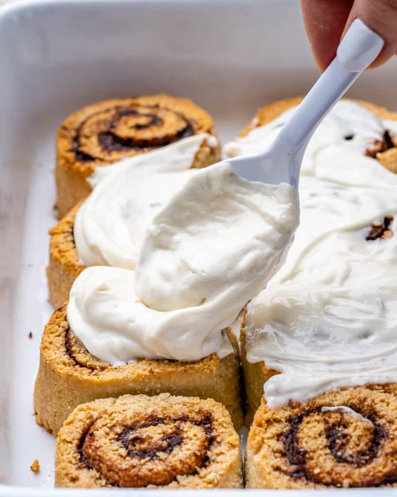 A pan of cinnamon rolls being topped with cream cheese glaze