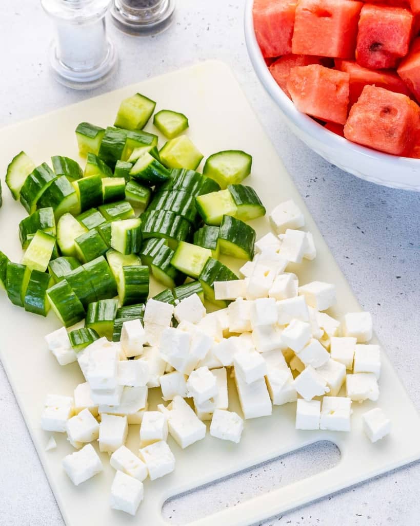 Cubed feta and watermelon with chopped cucumbers on cutting 