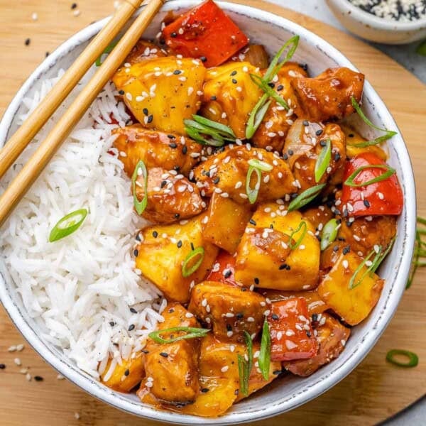 a bowl with rice topped with sweet and sour chicken made with bell pepper and pineapples.