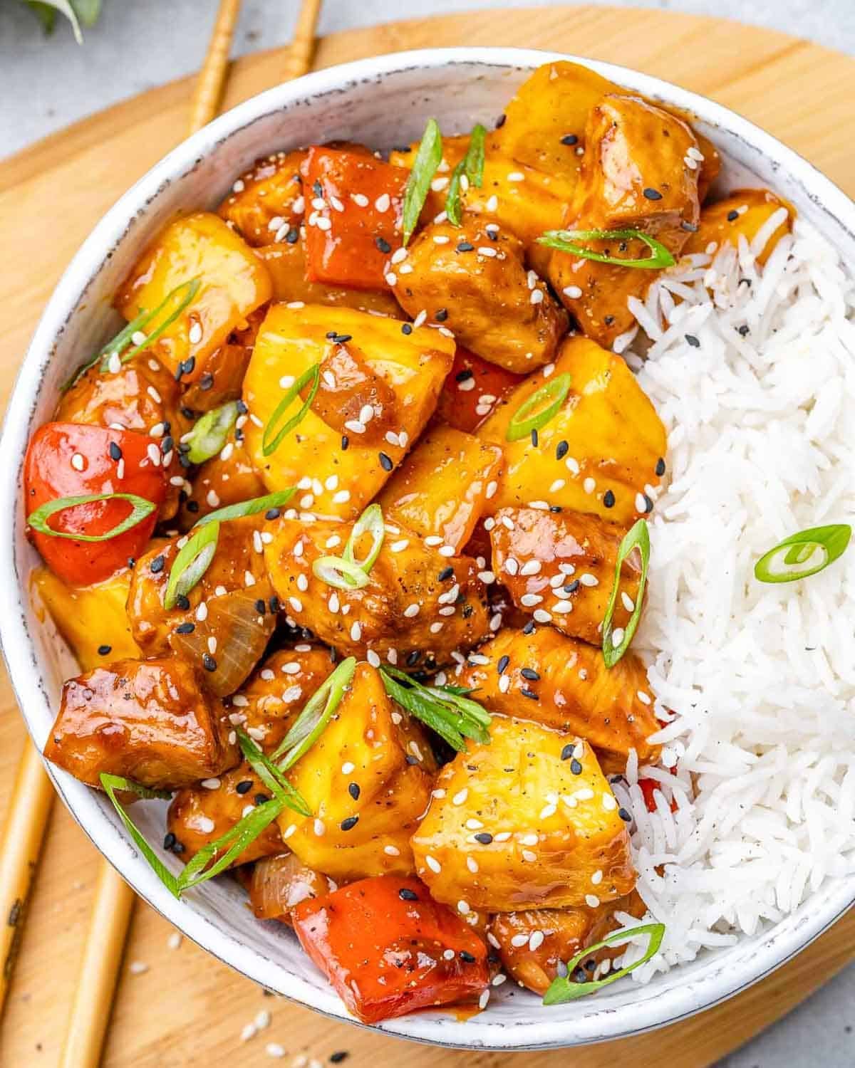 sweet and sour chicken in a bowl with veggies and pineapple served over rice. 