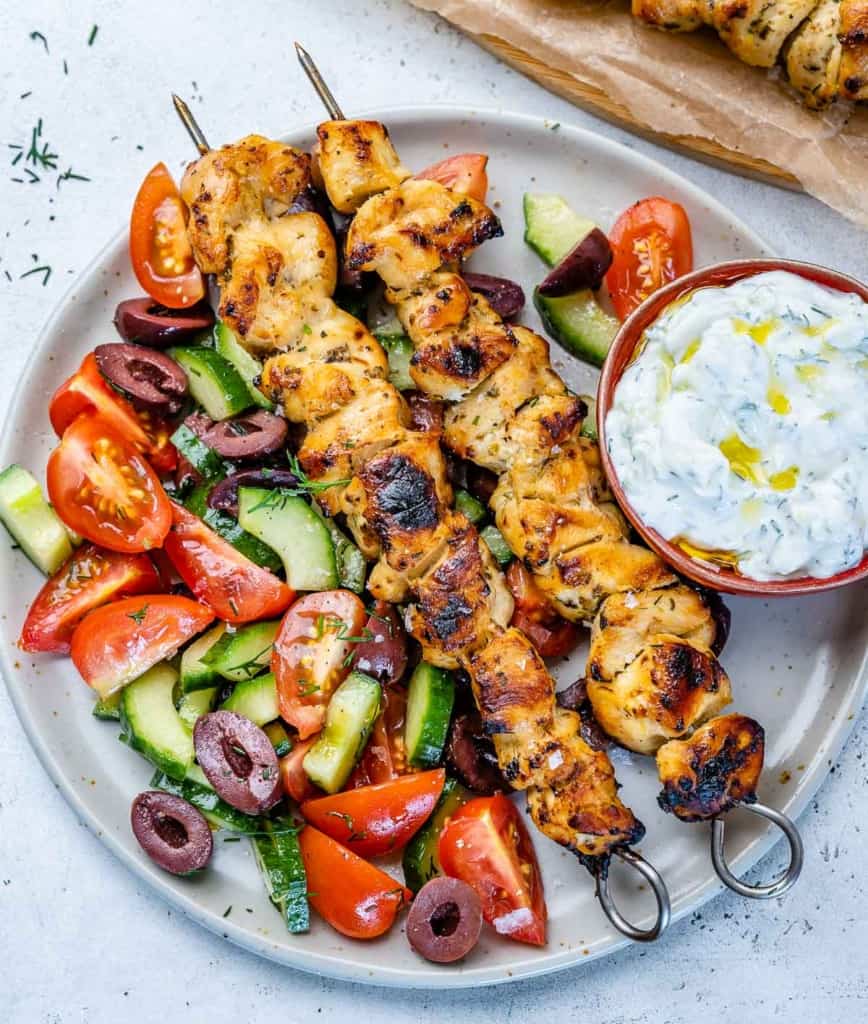top view of chicken souvlaki on white plate with vegetables 
