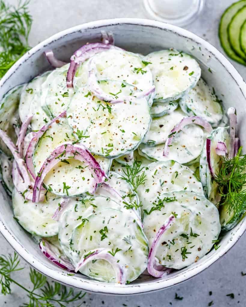 top view cucumber salad in a white bowl with herbs and purple onion