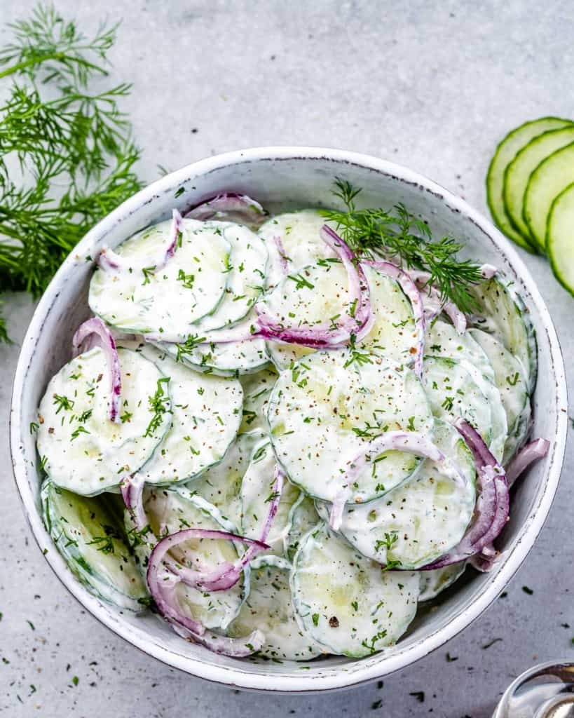 top view creamy looking cucumber salad with red onions, and topped with fresh dill