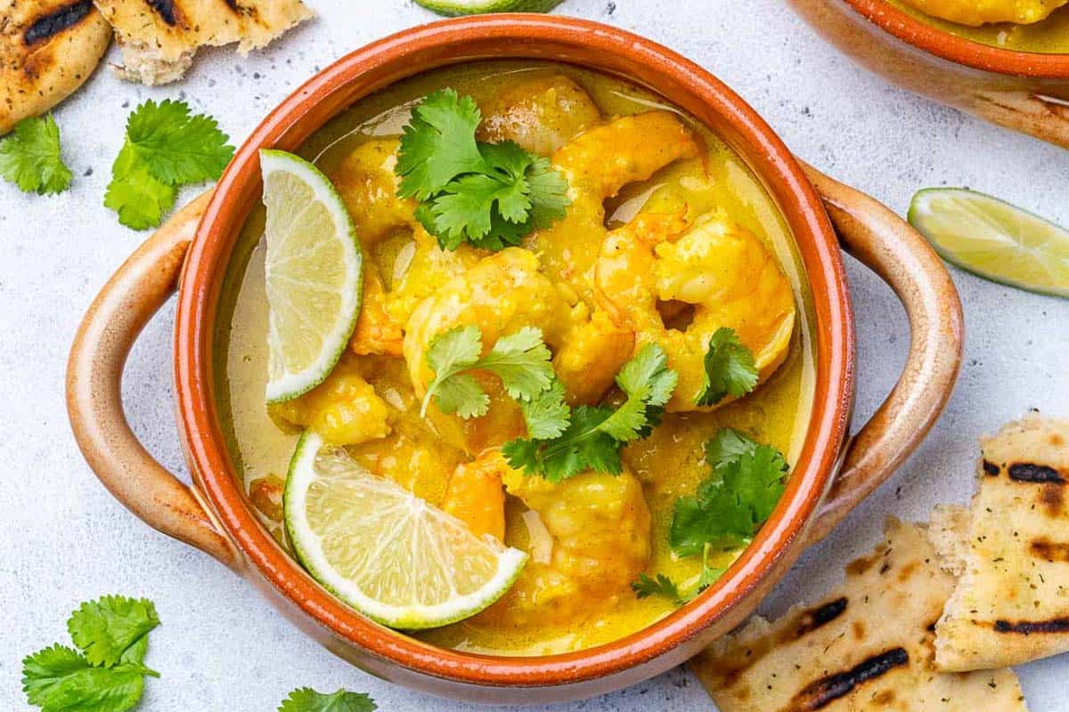 a round dish filled with green curry shrimp topped with fresh cilantro.