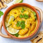 a round bowl with green curry shrimp topped with lime slices and cilantro.