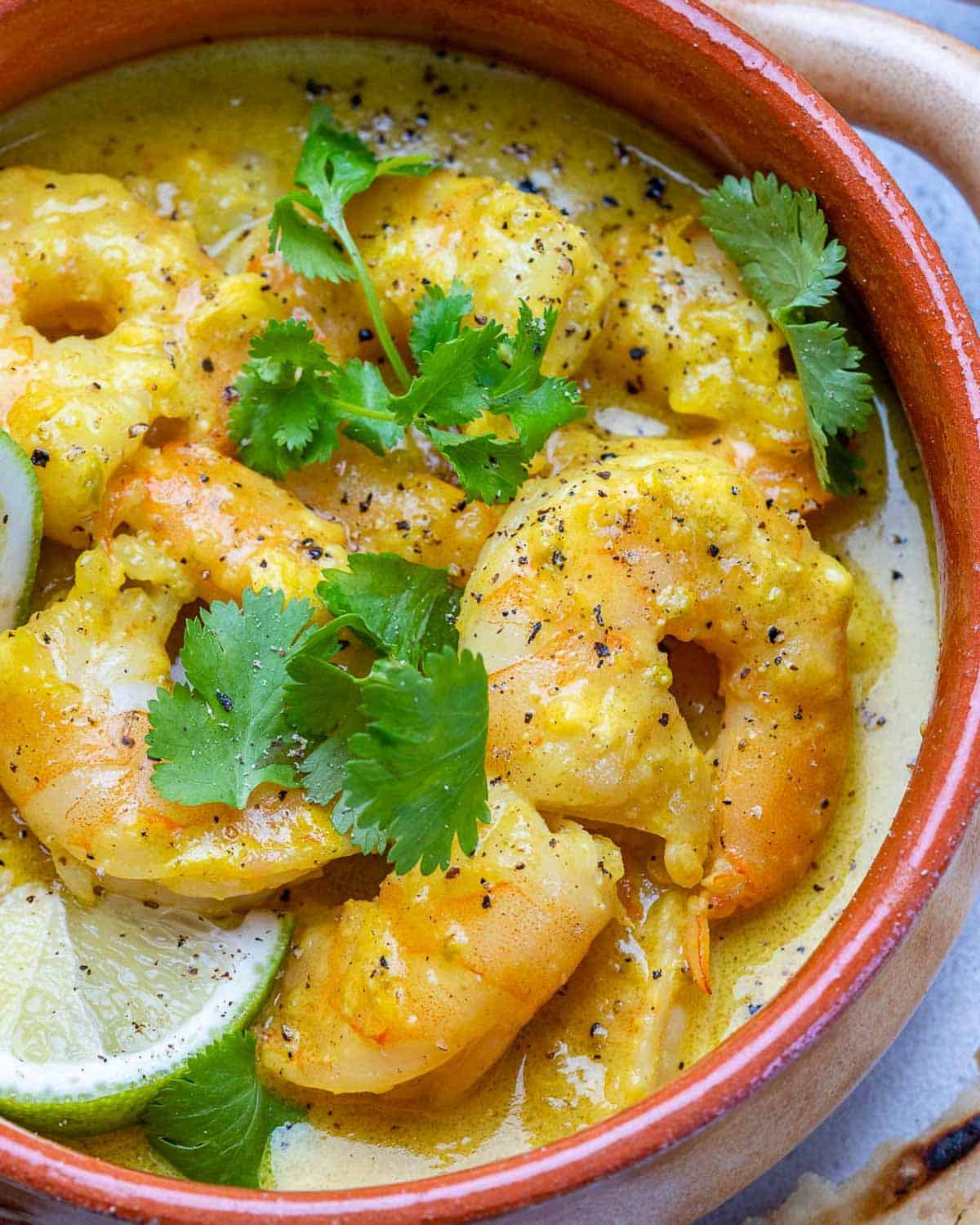 shrimp seared in green curry sauce in a bowl topped with fresh cilantro and lime wedges.