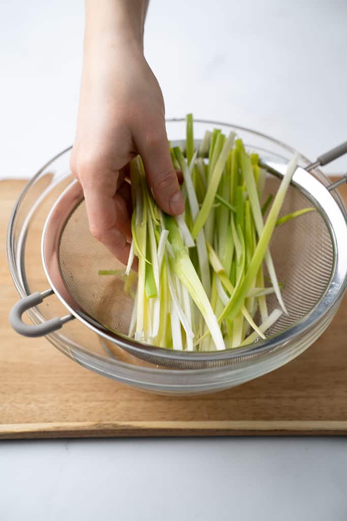Sliced leeks placed in a mesh strainer.