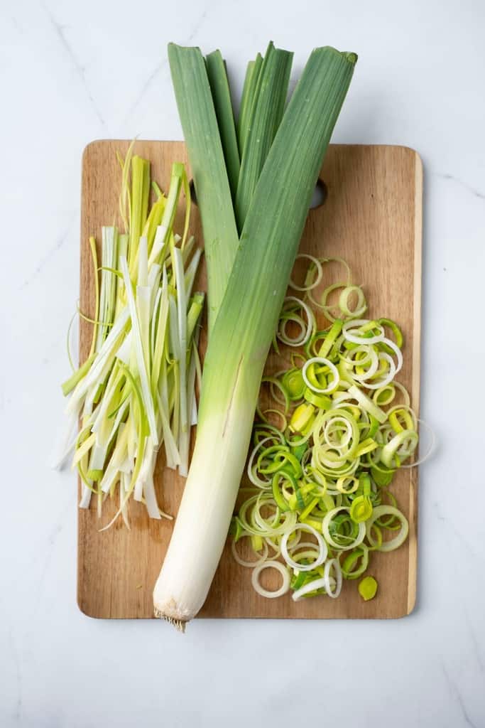 Leek on a cutting board with different cuts beside it.