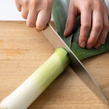 hand slicing the leek in half with a knife