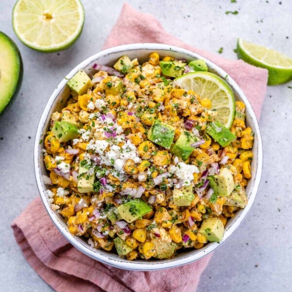 a round bowl over a napkin with street corn salad and half a lime next to the bowl.