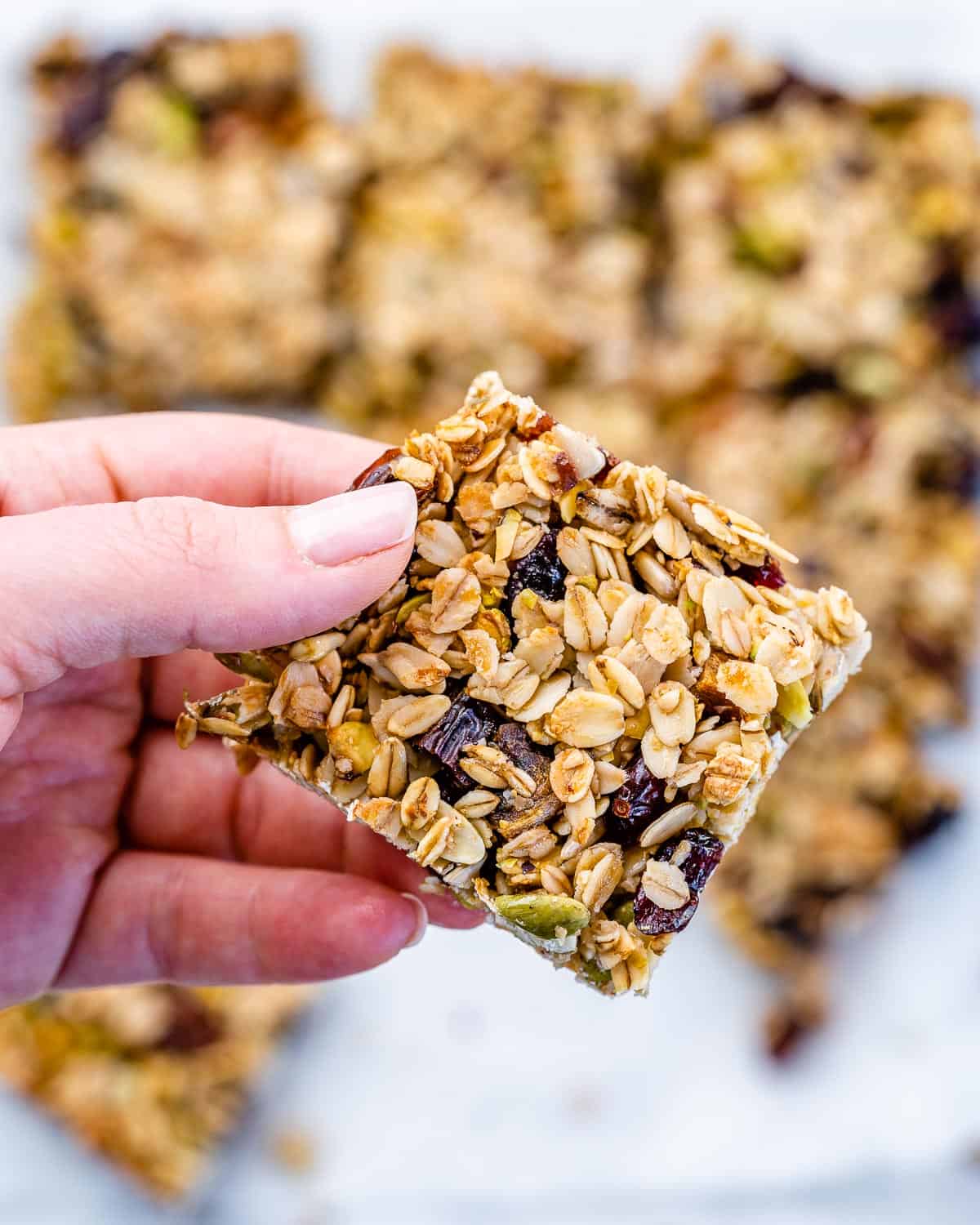 Oatmeal Granola Bars from Scratch 6 A hand gently holds a single homemade oatmeal granola bar, showcasing its inviting chewiness and the visible mixture of oats, nuts, and dried fruits.