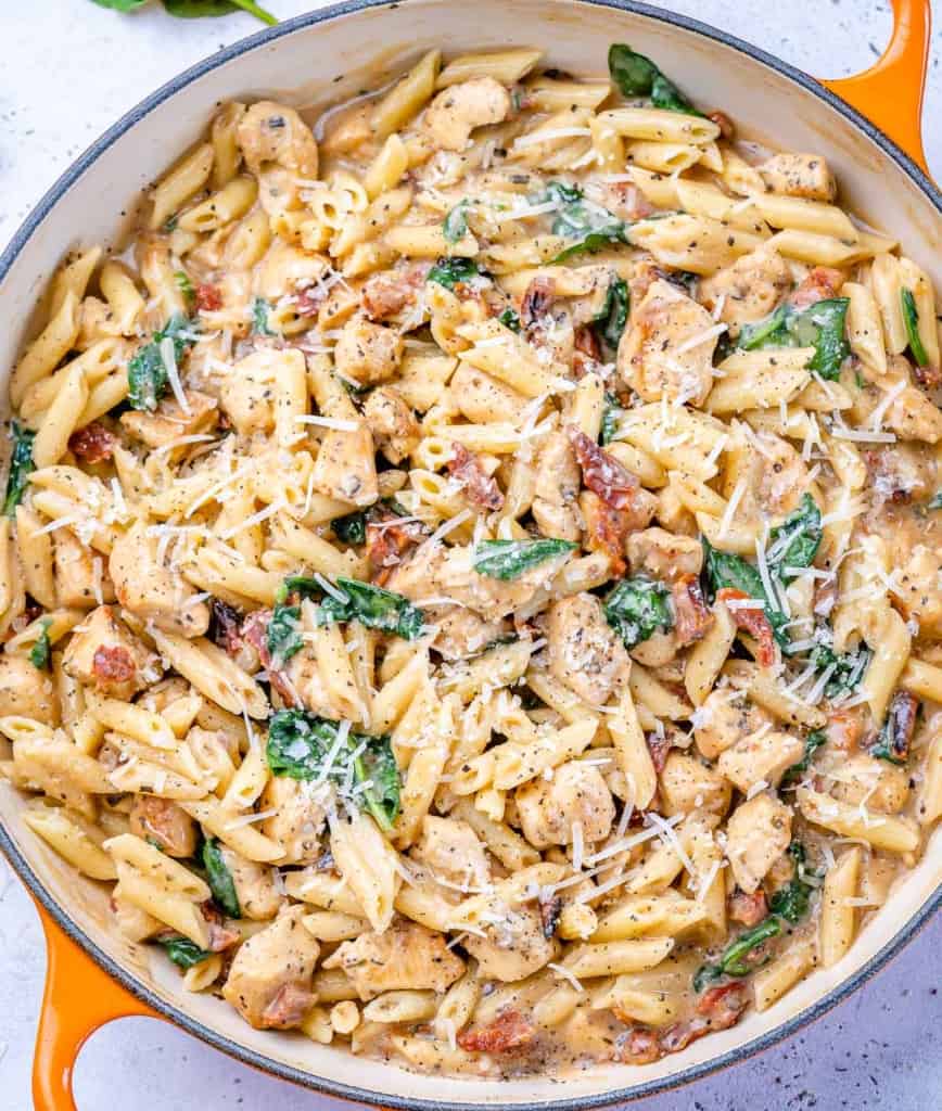 top view chicken pasta with spinach in an orange skillet