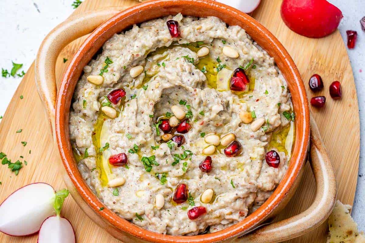 baba ganoush in a bowl topped with pomegranate arils and pine nuts.