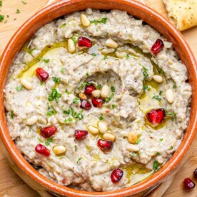 roasted eggplant dip in a bowl topped with pine nuts and parsley with a drizzle of olive oil.