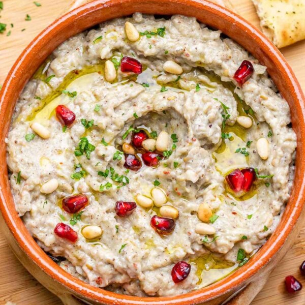 roasted eggplant dip in a bowl topped with pine nuts and parsley with a drizzle of olive oil.