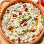 baba ganoush in a brown round bowl topped with pine nuts and pomegranate arils.