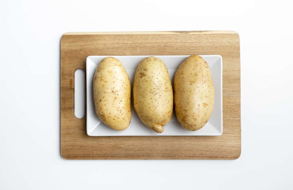 three potatoes on wooden cutting board