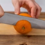 side shot image of a knife slicing the top of an orange