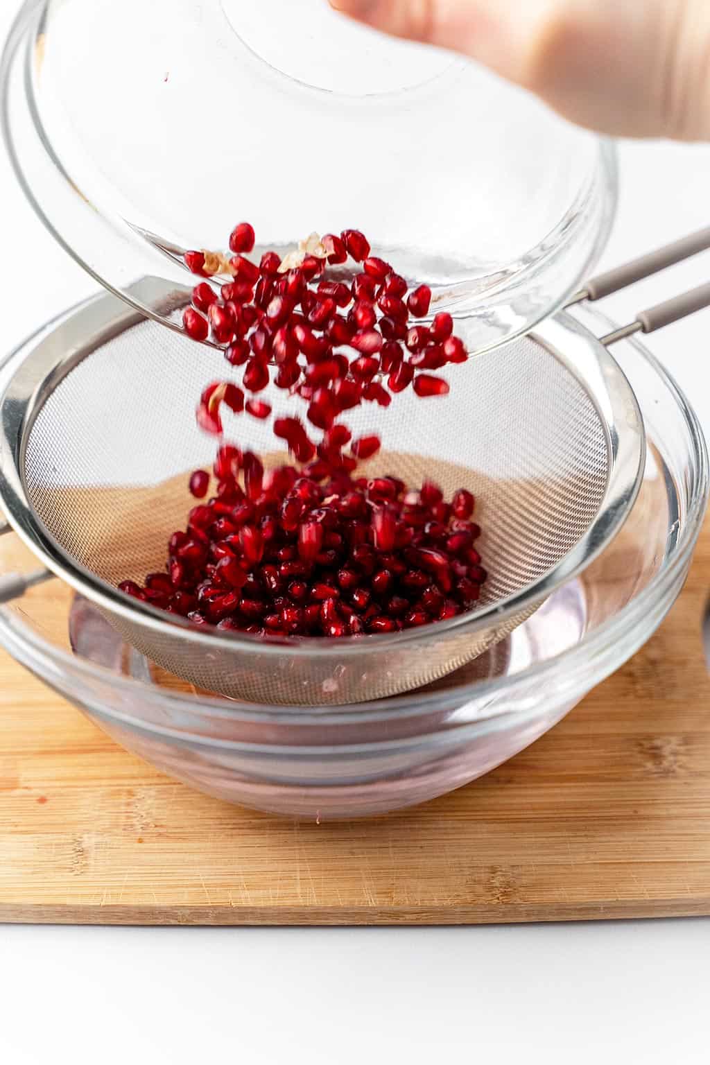 pouring pomegranate arils in mesh strainer over water