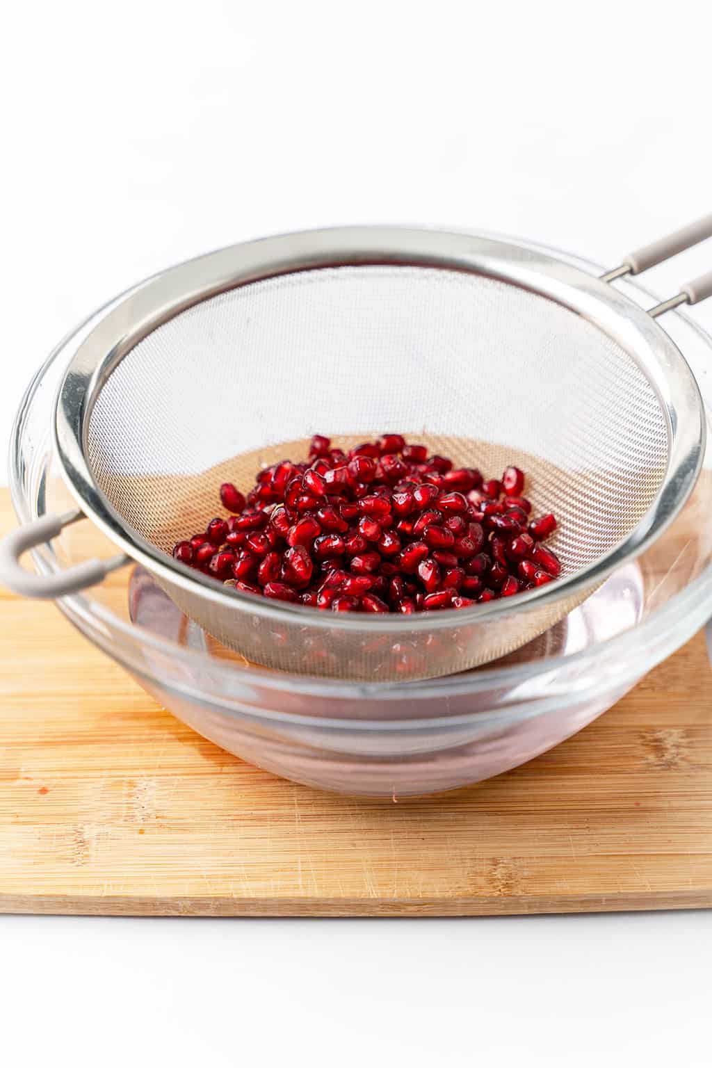 pouring pomegranate arils in mesh strainer over bowl of water to clean