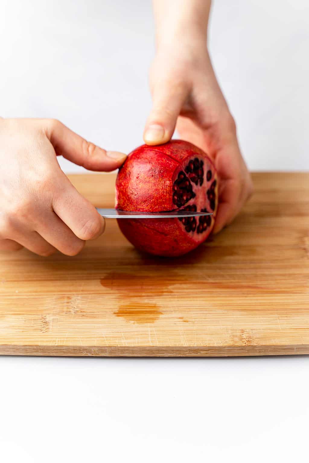 slicing the pomegranate skin with a knife on cutting board