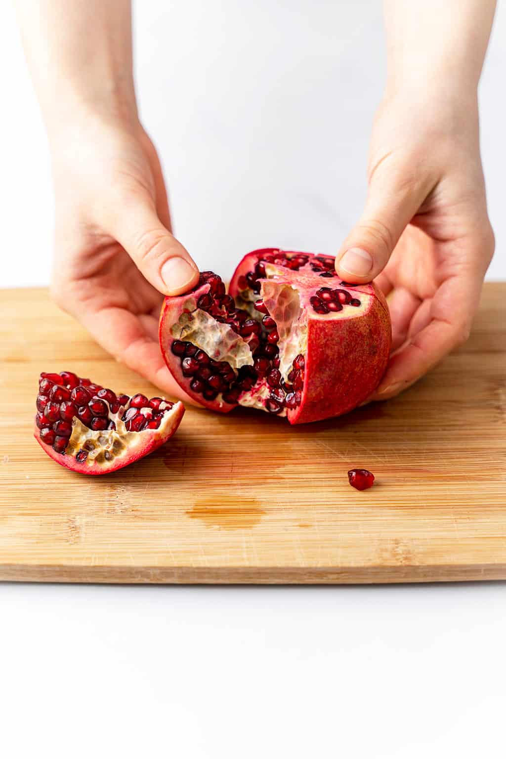 pulling the pomegranate in half with hands on cutting board