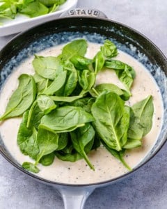 spinach added in a creamy sauce in a pan.