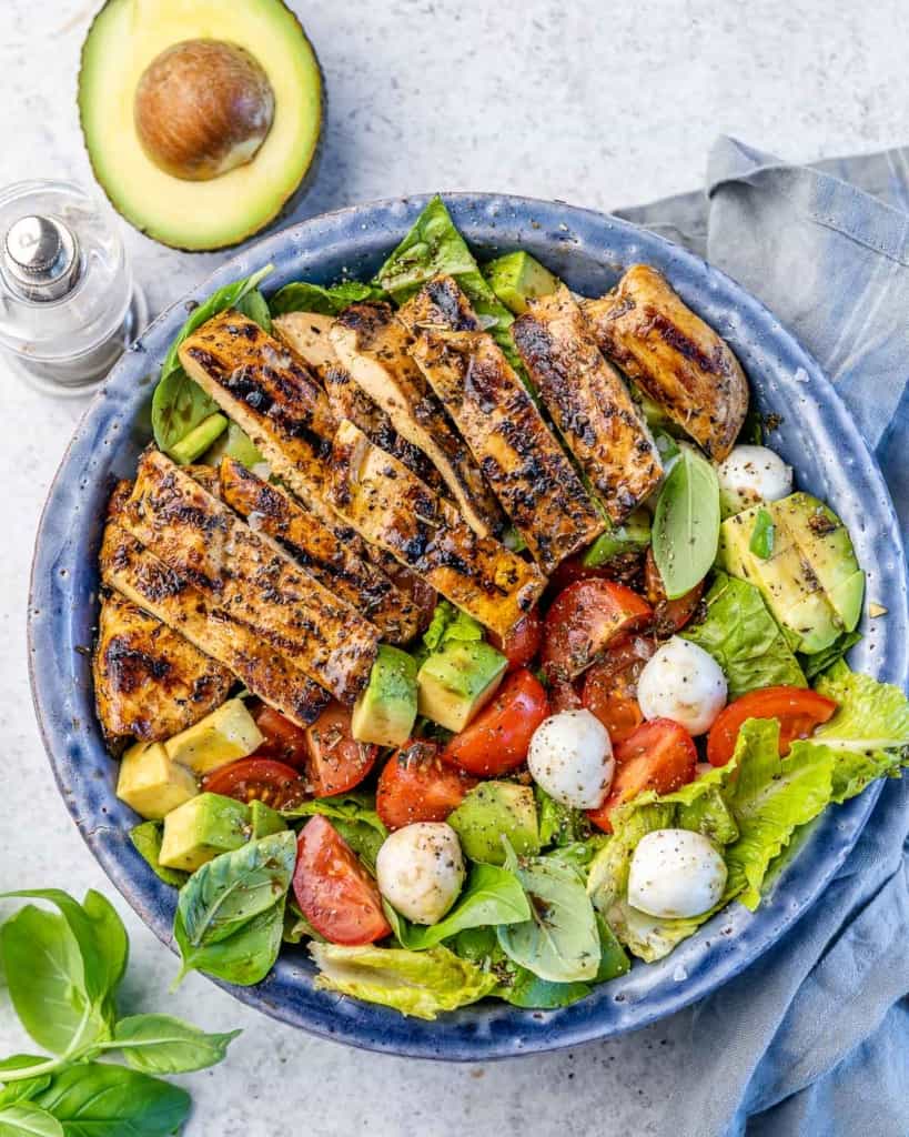 top view or chicken salad in blue bowl with avocado and fresh basil on side  