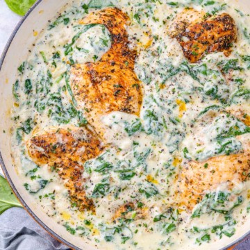 top view creamy chicken breast with spinach in an orange skillet