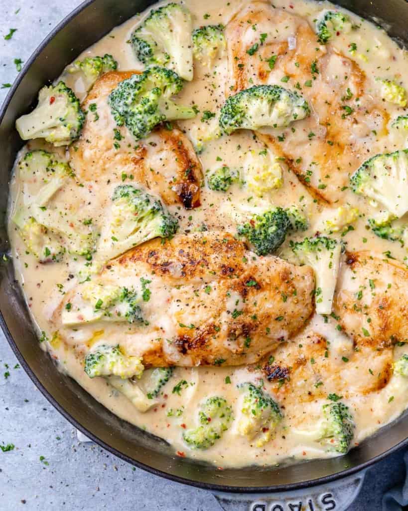 top view creamy chicken breast with broccoli in a black skillet
